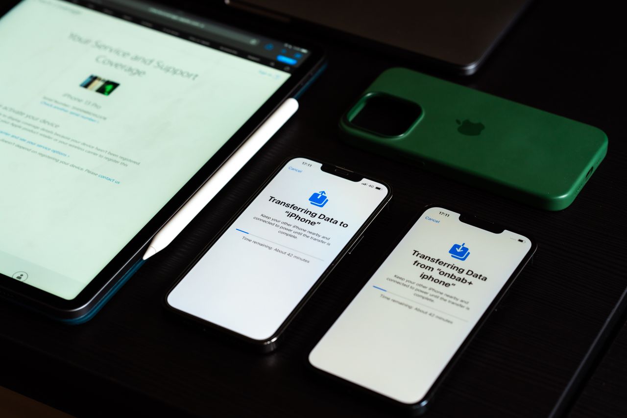 High-angle view of digital devices including iPhones and an iPad on a desk, showcasing data transfer.